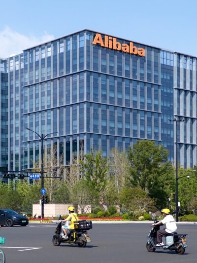 A group of people riding scooters in front of alibaba building