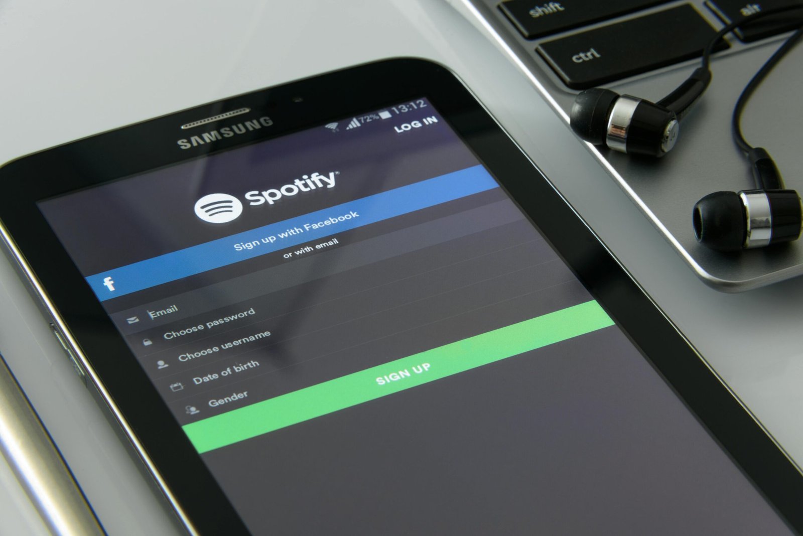 Smartphone showcasing Spotify login screen beside laptop and earphones on desk.